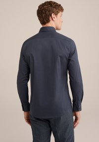 Camisa de manga larga azul marino con cuello puntiagudo, detalle en la yoke trasera y puños abotonados. Tejido suave con un corte ajustado.