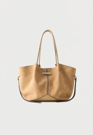 Lichtbruine suède tote bag met lange dubbele hengsels, licht ingezakte vorm, zwarte rand en een klein metalen merkplaatje middenvoor.