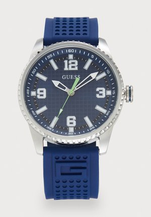 Montre avec un bracelet en silicone bleu, un boîtier en acier inoxydable argenté, un cadran bleu texturé, des index des heures audacieux et une aiguille des secondes verte.