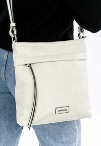 Hvid læder crossbody taske med en foldet top, sorte accentdetaljer og en sølvfarvet logo-plade. Har justerbar strop og glat tekstur.