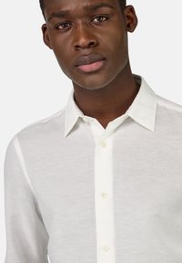 Camicia bianca di lino con colletto classico, dotata di una chiusura con bottoni sul davanti e una texture sottile. Tessuto morbido e design leggero.