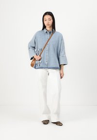 Denimskjorta med långa ärmar och knappstängning; har fickor med klaff och rosett detaljer. Matchas med vita utsvängda byxor och leopardmönstrade ballerinaskor.