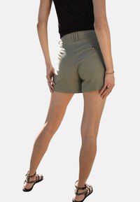 Shorts vert olive avec une coupe ajustée, présentant une taille haute, une poche arrière avec un détail de bouton doré et une texture de tissu lisse.