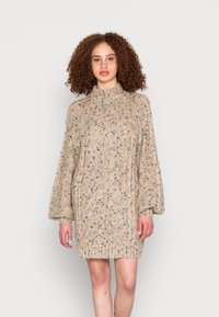 Vestido de malha em bege, com um padrão texturizado, gola alta e mangas balão soltas, com manchas de preto e castanho.