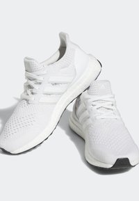 Vitaidrottsskor i vitt med ovandel i stickat, tre vita ränder på sidan och en texturerad sula. Har en vadderad mellansula och snörningsdesign.