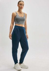 Top corto gris combinado con pantalones de chándal azul oscuro que tienen una cinturilla elástica y bolsillos laterales, usados con zapatillas deportivas blancas.