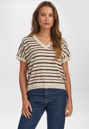 Beige V-hals gestreept shirt met donkerbruine strepen, korte mouwen en een ontspannen pasvorm. Gedragen met donkerblauwe denimjeans.