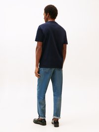 T-shirt bleu marine à manches courtes avec un col rond, associé à un jean en denim bleu clair, avec des ourlets retroussés, et des chaussures noires, vu de l'arrière.