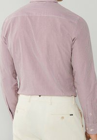 Chemise à manches longues rayée rouge et blanche avec des détails boutonnés, associée à un pantalon beige clair, présentant un empiècement au dos et des poignets contrastants.