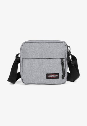 Harmaa kangasolki-toimituskassi, jossa on suuri pääosasto, etupussukka vetoketjulla, musta hihna ja punainen Eastpak-logopatch. Suorakulmainen muoto.