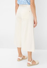 Pantalons large beige clair avec poches arrière, dotés d'une taille haute et d'un matériau en coton doux. Associés à des sandales espadrilles légères.