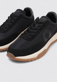 Zapatillas negras con una combinación de texturas lisas y de gamuza, con un logo sutil, puntera redondeada y suela de goma.