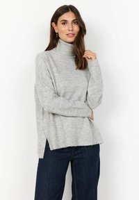 Light grey turtleneck sweater with a relaxed fit, ribbed cuffs, side slits, and a soft texture. Paired with dark blue wide-leg jeans.