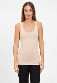 Beige tank top with a scoop neck, made of soft, stretch fabric. Features wide shoulder straps and a fitted design. Worn with black pants.