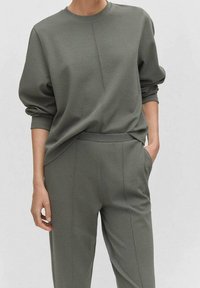 Sweat-shirt vert olive avec épaules tombantes et poignets côtelés, associé à un pantalon fuselé assorti avec poches latérales et détails de couture.