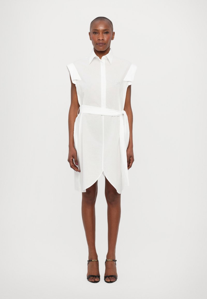 White shirt dress with short sleeves, button front, belted waist, and asymmetrical hemline. Made from lightweight, translucent fabric.