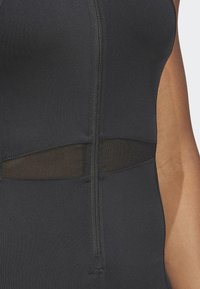 Black athletic bodysuit with a zip closure, featuring a sheer mesh panel at the waist. Smooth texture and fitted design.
