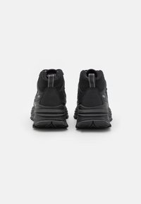 Zapatillas deportivas negras con upper texturizado, cuello acolchado y suela de goma con un diseño único y acentos en el tacón. Vista trasera mostrada.