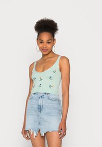 Top cropped verde claro com bordado floral, combinado com uma mini saia de ganga clara com a bainha desfiada e abertura frontal.