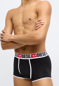 Boxeri negri cu margini albe și talie cu logo, având text roșu și negru. Confecționați din material moale și elastic.