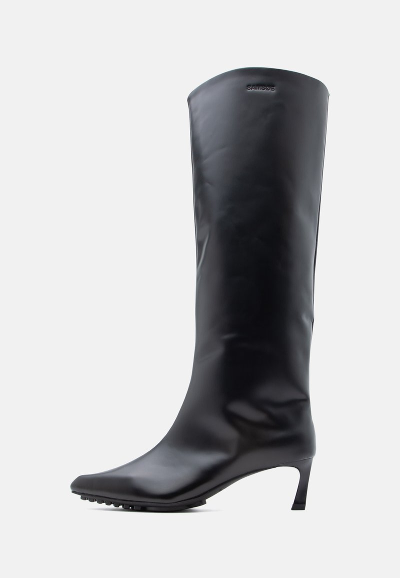 Botte en cuir noire montant jusqu'au genou avec un bout pointu et un talon haut et mince. Texture lisse avec un minimum de métal et le logo de la marque près du haut.