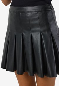 Črna usnjena krilo z naborki, gladke teksture in oprijetim pasom, opremljeno z zadrgo na strani za enostavno oblačenje.