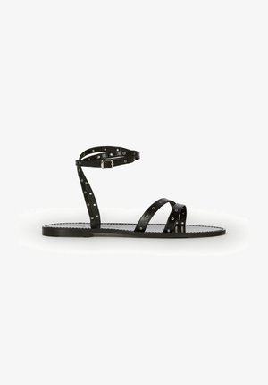 Black flat sandal with thin straps featuring silver eyelets, one around the ankle with a buckle and two crossing over the toes.