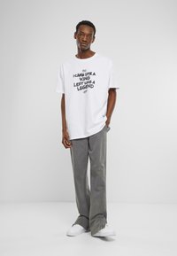 T-shirt en coton blanc avec des graphismes noirs audacieux : "Je suis venu comme un roi, je suis parti comme une légende." Assorti avec un pantalon large gris et des baskets blanches.