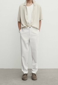 Korte mouwen, beige, gestructureerde knoopshirt met een kraag, gecombineerd met witte broek en bruin veterschoenen. Eenvoudig en schoon ontwerp.