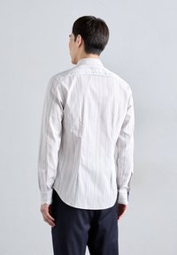 Camisa de manga larga a rayas en blanco con líneas azul claro y naranja, con un dobladillo curvado, puños de un botón y una textura suave de algodón.