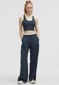 Donkerblauwe sportieve crop top met geribbelde textuur, gedragen met een losvallende donkerblauwe joggingbroek met elastische tailleband en zijzakken.