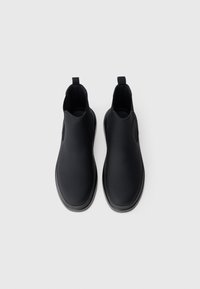 Sorte ankelstøvler i glat syntetisk materiale med en rund tå, minimalistisk design, elastiske sidelapper og stropper på hælen.