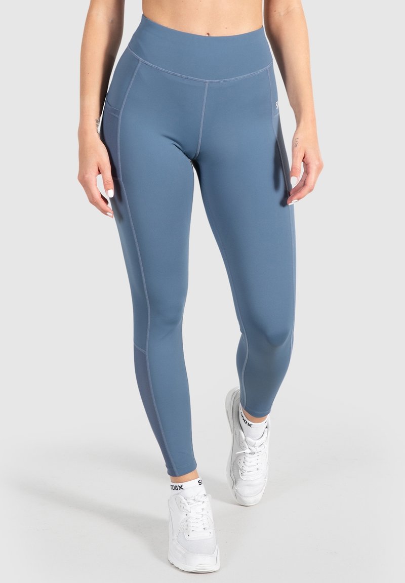 Højtaljede leggings i en dæmpet blå nuance, lavet af strækbart stof. Har sidelommer og kontrasterende syninger.