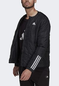 Zwarte pufferjack met een rits aan de voorkant, voorzien van een gestikte textuur, witte drie-strepen accenten op de mouwen en een Adidas-logo op de borst.