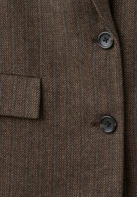 Manteau marron à motif chevrons avec fines rayures bleues, doté de deux boutons noirs et d'une poche à rabat sur le côté gauche.