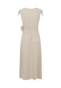 Robe midi beige sans manches avec bretelles nouées aux épaules, taille élastique et détail fleur en tissu sur le côté droit.