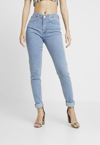 Jeans de tiro alto en azul claro con corte ajustado, cinco bolsillos y dobladillos remangados, combinados con sandalias de tacón con estampado de serpiente marrón.