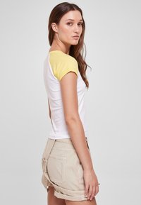 Kortermet T-skjorte med hvit kropp og gule ermer, kombinert med beige shorts. Laget av bomull, tettsittende design, glatt tekstur.