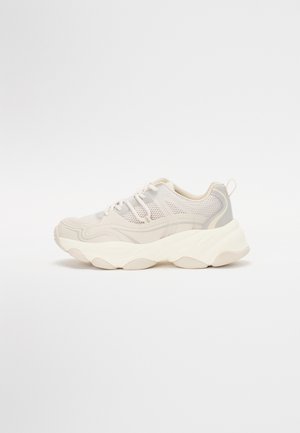 Sneakers met een lichtbeige mesh bovenwerk, ronde neus en een robuuste witte zool met golvende patronen. Voorzien van roze veters en een trekband.