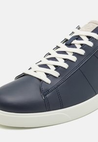 Baskets en cuir bleu foncé avec lacets blancs et semelle blanche, montrant une couture détaillée et une étiquette beige sur la languette.