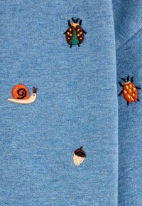 Tessuto a maglia blu con disegni ricamati di due coccinelle, una lumaca e una ghianda, con colori e texture variegati.