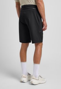 Schwarze Sportshorts mit glatter Textur, elastischem Bund mit Logo und Seitentaschen. Stylisch kombiniert mit weißen Socken und hellen Sneakers.