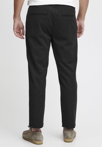 Pantalons gris foncé à coupe slim, présentant un tissu légèrement texturé, deux poches arrière et des poignets à la cheville.