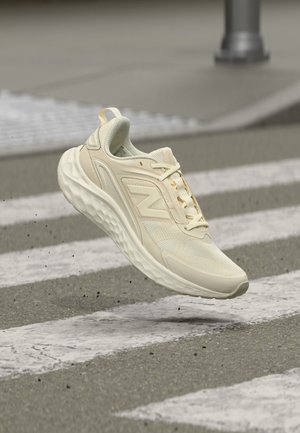Бежов спортен обувка New Balance с омекотена подметка във въздуха над пешеходна пътека на асфалтовата улица.