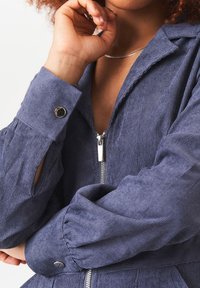 Navy ribbed jumpsuit featuring a zip front, button cuffs, and soft texture; details include a collar and gathered sleeves.