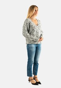 Suéter de punto gris y blanco con escote en V, patrón texturizado, mangas anchas, combinado con jeans azul claro y tacones de punta negra.