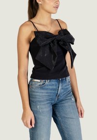 Zwart mouwloos topje met een grote pailletten strik aan de voorkant. Gecombineerd met lichtblauwe denim jeans met slijtageplekken. Eenvoudig, aansluitend ontwerp.