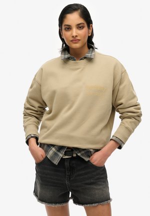 Beige sweatshirt met ribgebreide manchetten en het logo "Superdry Saint Tropez". Draag het over een gelaagde geruite shirt en combineer het met donkere denim shorts.