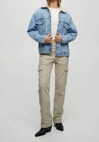 Vaaleansininen farkkutakki, jossa on valkoinen turkiskaulus, yhdistettynä beigeihin cargo-housuihin. Mustat korkokengät täydentävät asua.