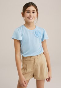 Top scurt cu maneci scurte, de culoare albastru deschis, cu un accent floral, asortat cu pantaloni scurți plisati bej, cu un nasture și șnur.